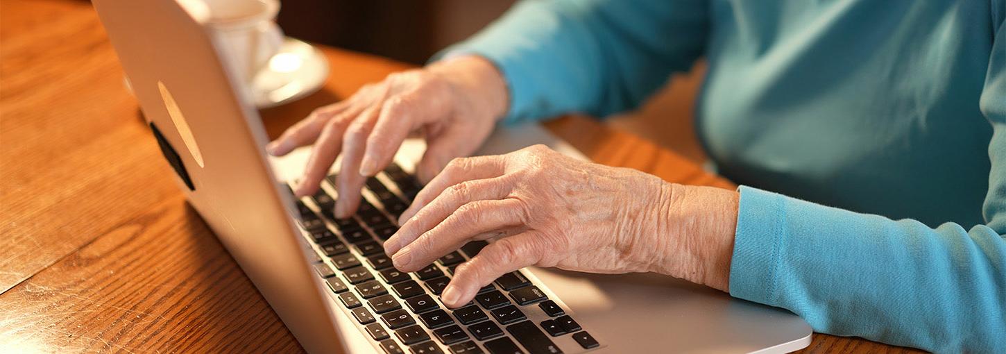 一位老妇人的手放在笔记本电脑的键盘上.